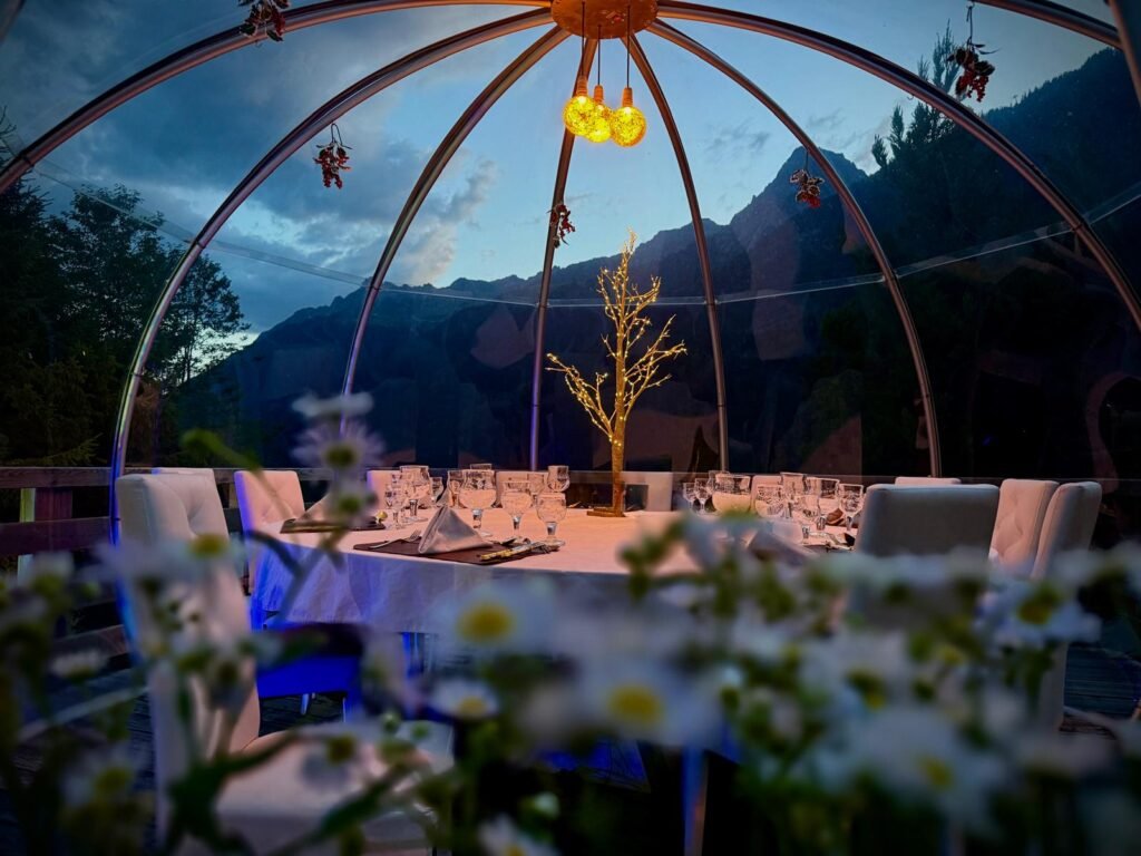 An inviting interior view of The Bubble of Philippe, showcasing its intimate and exclusive setting with elegant table arrangements, ambient lighting, and the stunning Chamonix valley visible through its transparent walls, ideal for private dining.